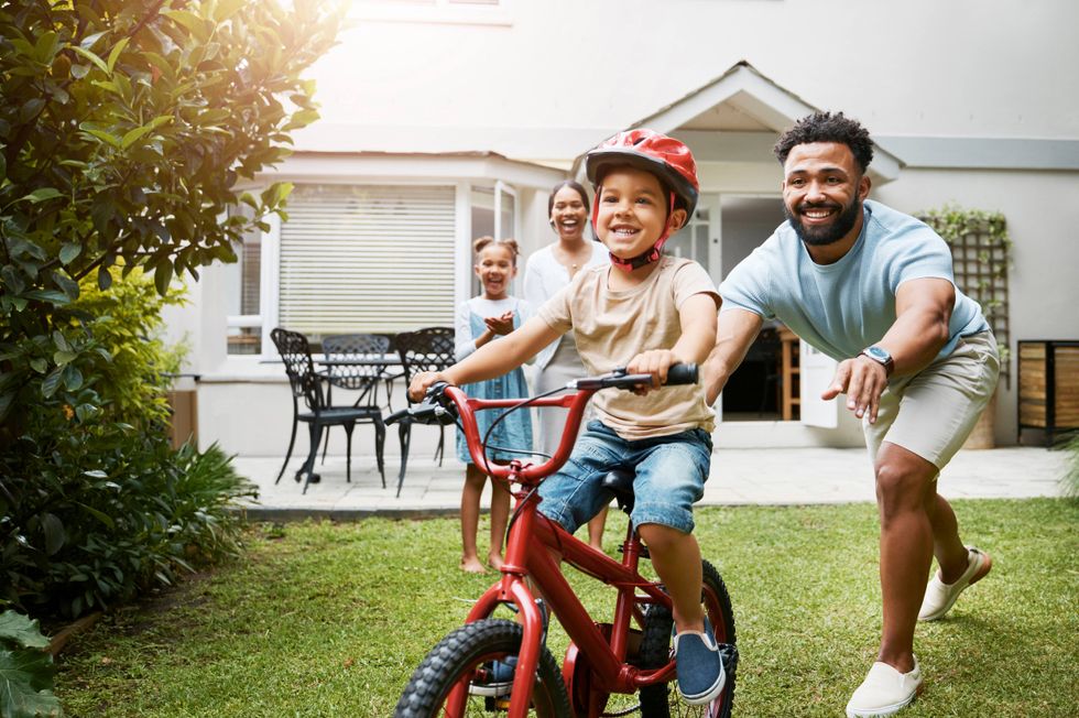 A family spends time together outdoors as a father helps a young child learn to ride a bicycle.