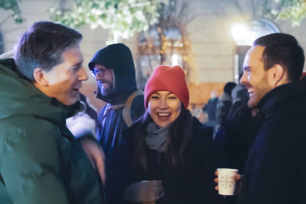A group of coworkers from Delivery Hero bundled in winter clothing, laughing and talking together outdoors. One woman in a red beanie smiles toward the camera while others chat around her.