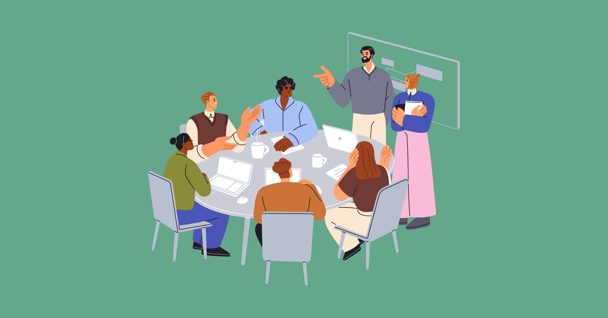 A group of diverse professionals sitting around a table with computers, papers, and coffee mugs while discussing a topic