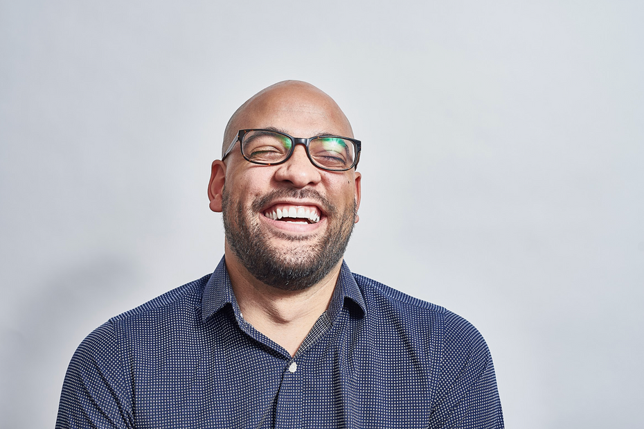 A man with glasses and a blue button down t-shirt laughing