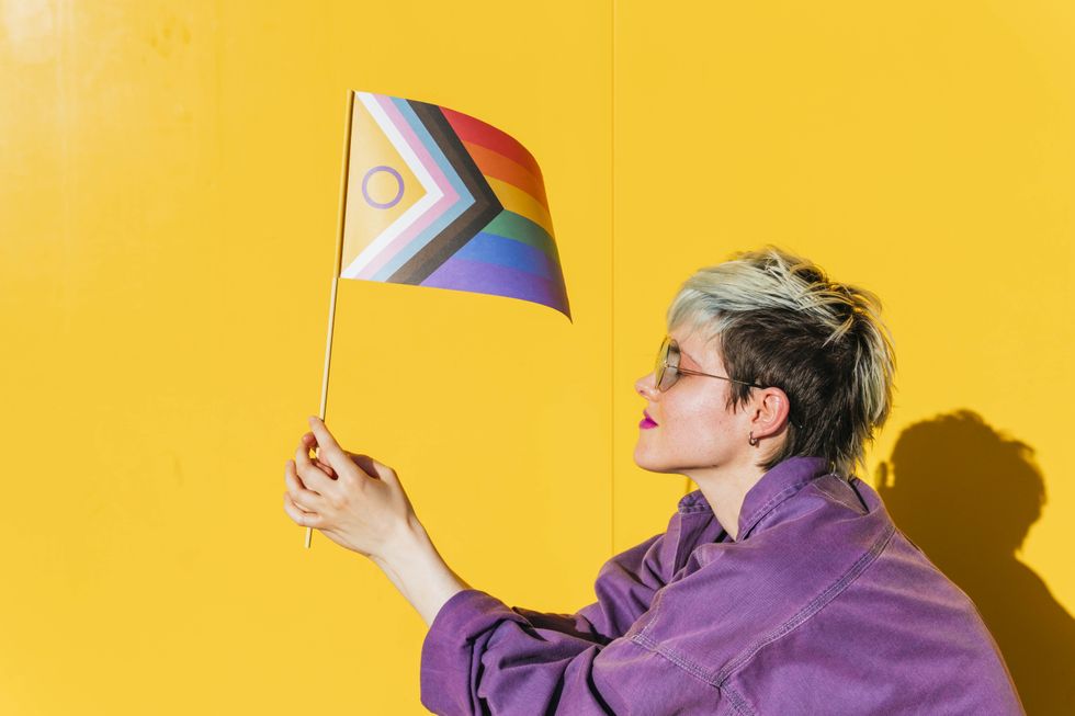 A person in a purple shirt with short hair holding a Pride flag