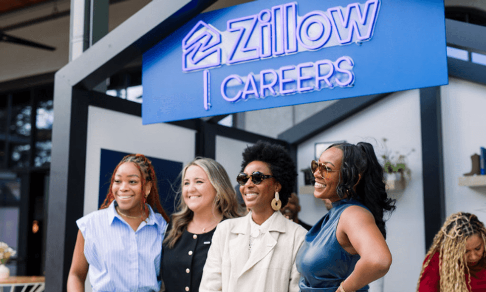 Employees posing together beneath a Zillow Careers sign at a recruiting or workplace event, representing community, company culture, and career opportunities at Zillow.