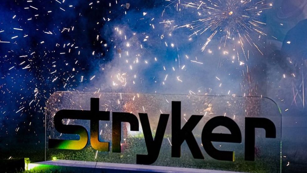 Fireworks bursting behind an illuminated Stryker sign during an outdoor celebration.