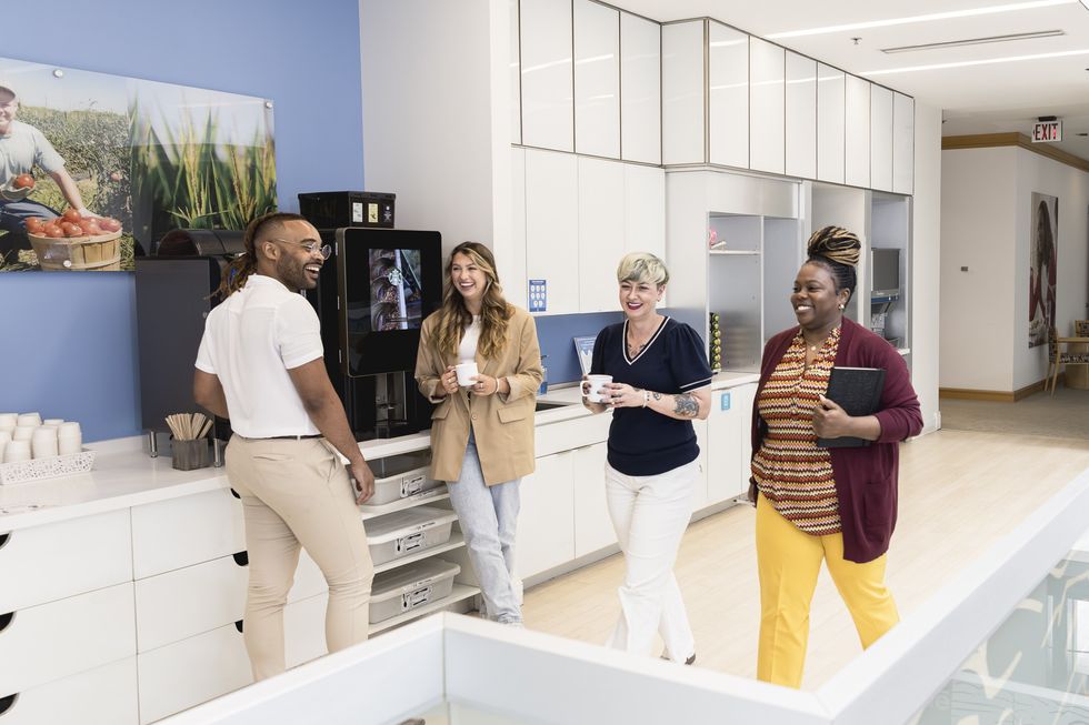 Four Nestle employees chatting and smiling in the breakroom over coffee.