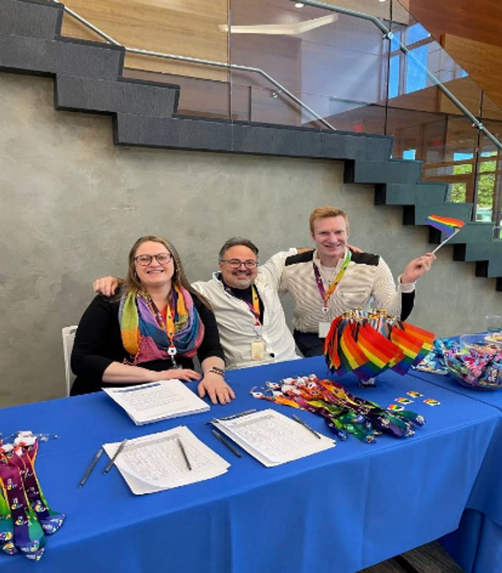 three people sitting at a table with Pride flags