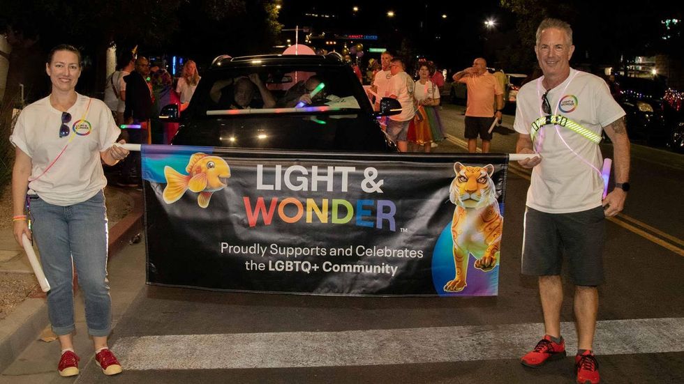 Two Light & Wonder teammates holding a sign that says "Light & Wonder proudly supports and celebrates the LGBTQ+ community"