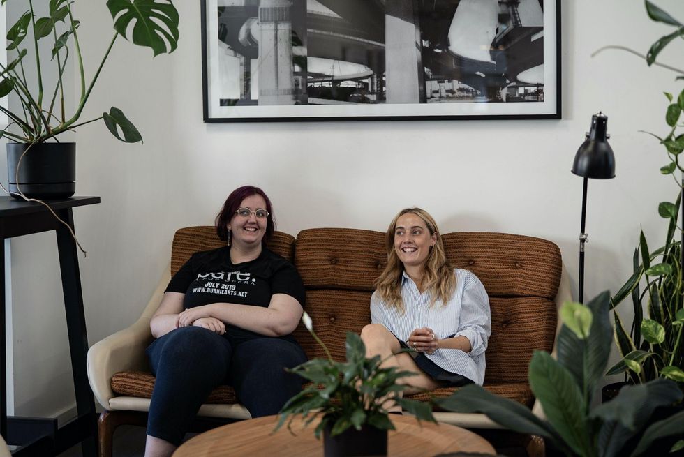 two women smiling sitting on a couch surrounded by plants