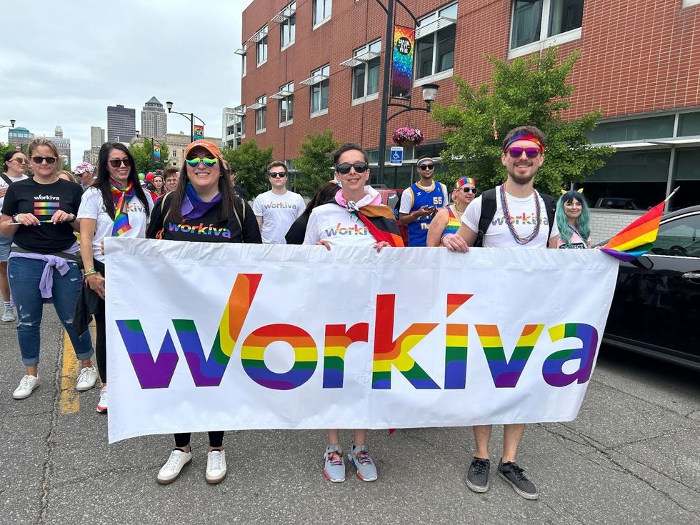 Various Workiva employees at a march holding a sign that says "Workiva" in Pride colors
